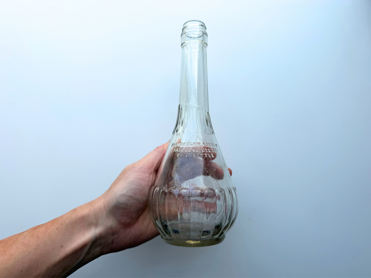 Hand holding a vintage ribbed clear glass genie bottle to show its scale and teardrop shape