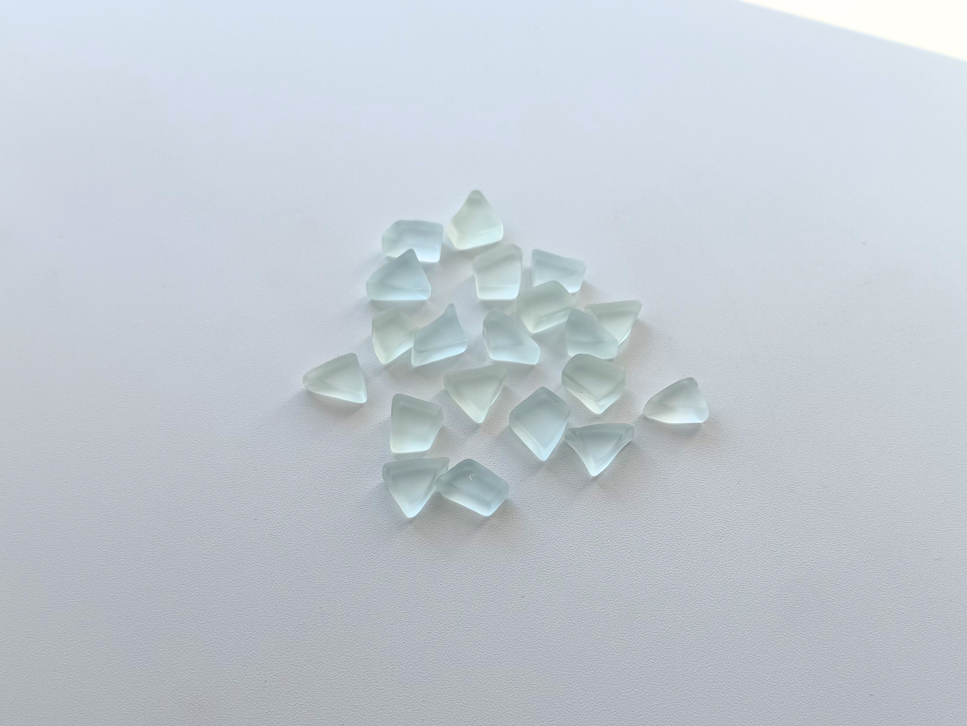 Loose pale blue and green tumbled sea glass pieces scattered on a white surface