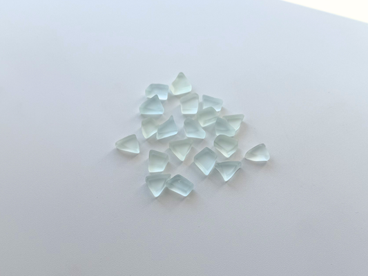 Loose pale blue and green tumbled sea glass pieces scattered on a white surface