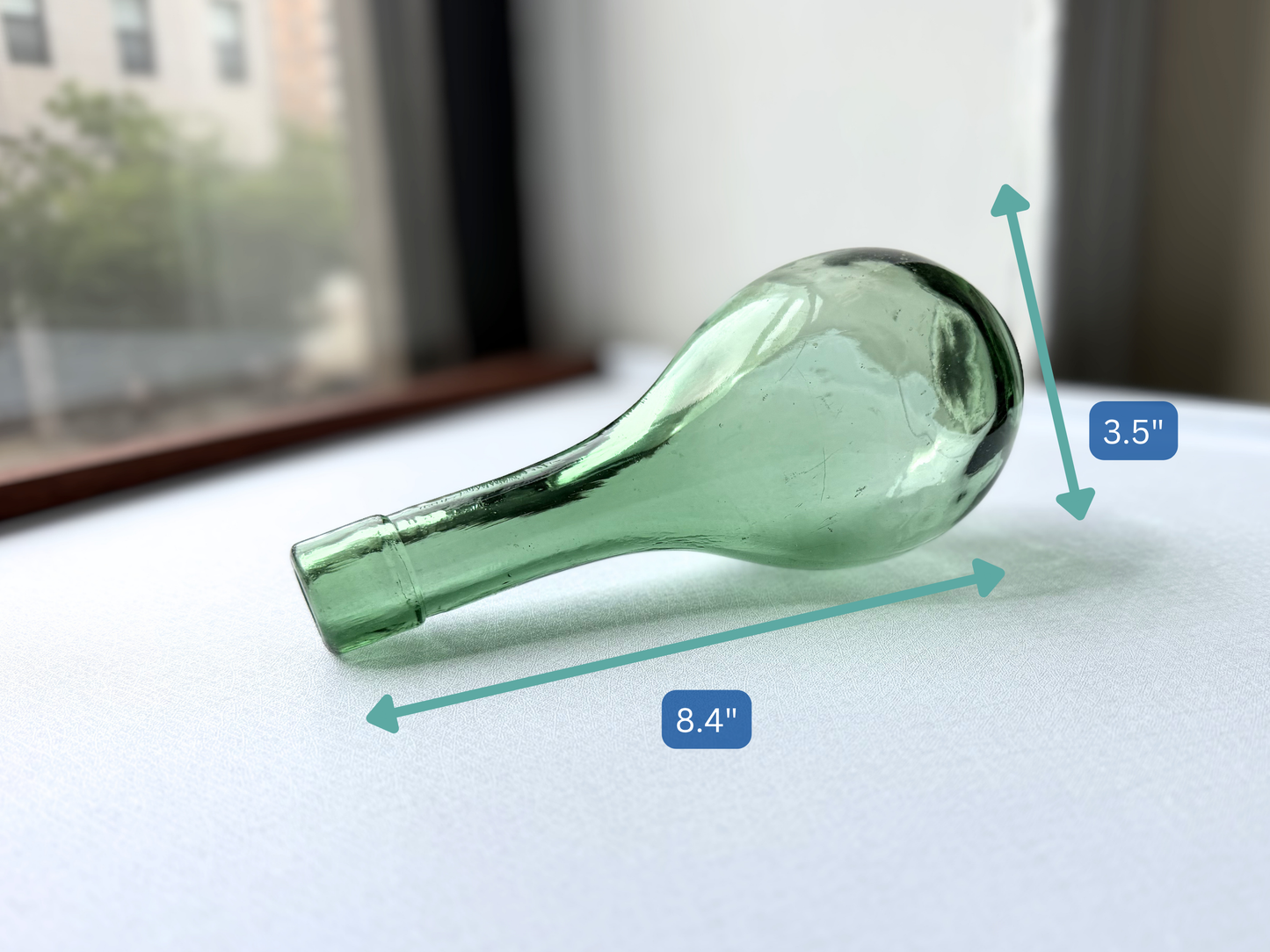 Angled view of a vintage green glass teardrop bottle highlighting the bubbles and asymmetry in the glass