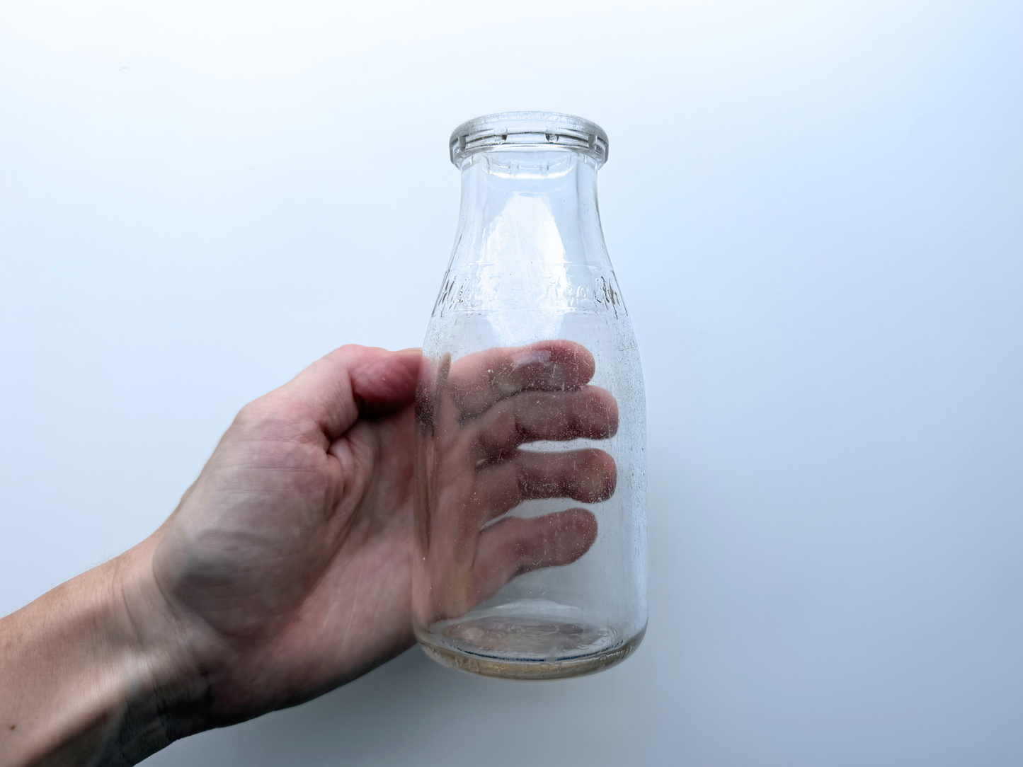 Hand reaching to hold a vintage clear glass Milk for Health milk bottle