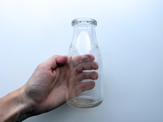 Hand reaching to hold a vintage clear glass Milk for Health milk bottle