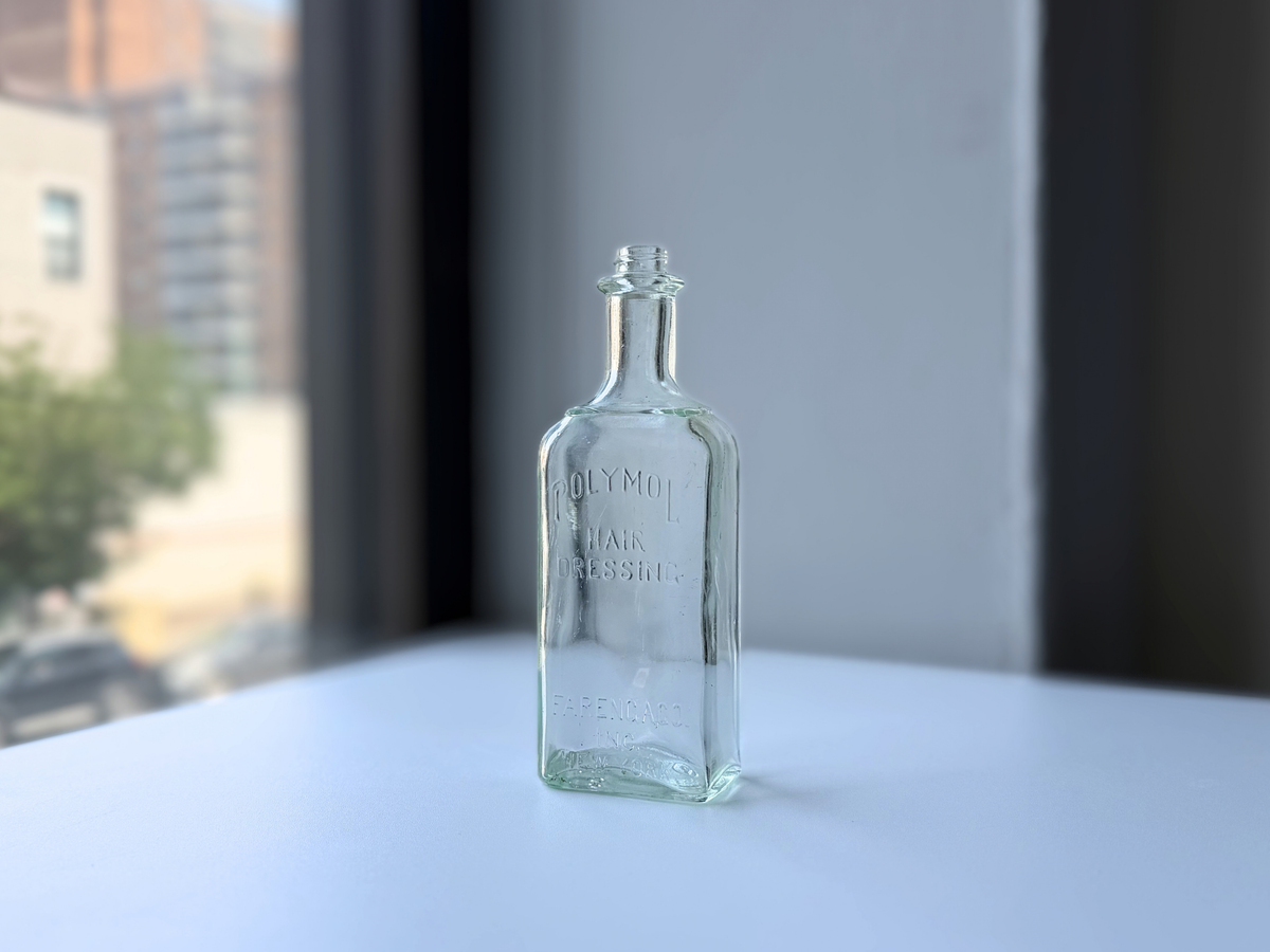 Vintage pale greenish-blue Polymol Hair Dressing bottle with embossed lettering on a sunny windowsill
