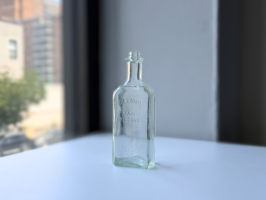 Vintage pale greenish-blue Polymol Hair Dressing bottle with embossed lettering on a sunny windowsill
