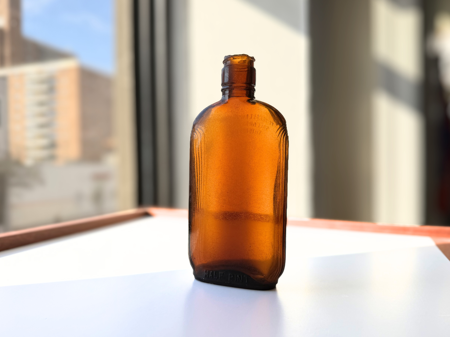 Sea-worn amber glass Art Deco flask shown upright against a bright window background