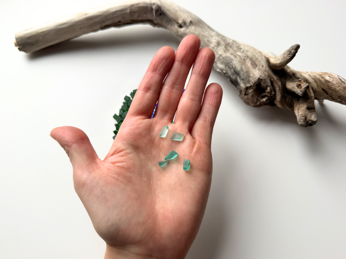 Hand holding scattered aqua micro sea glass pieces to show scale.