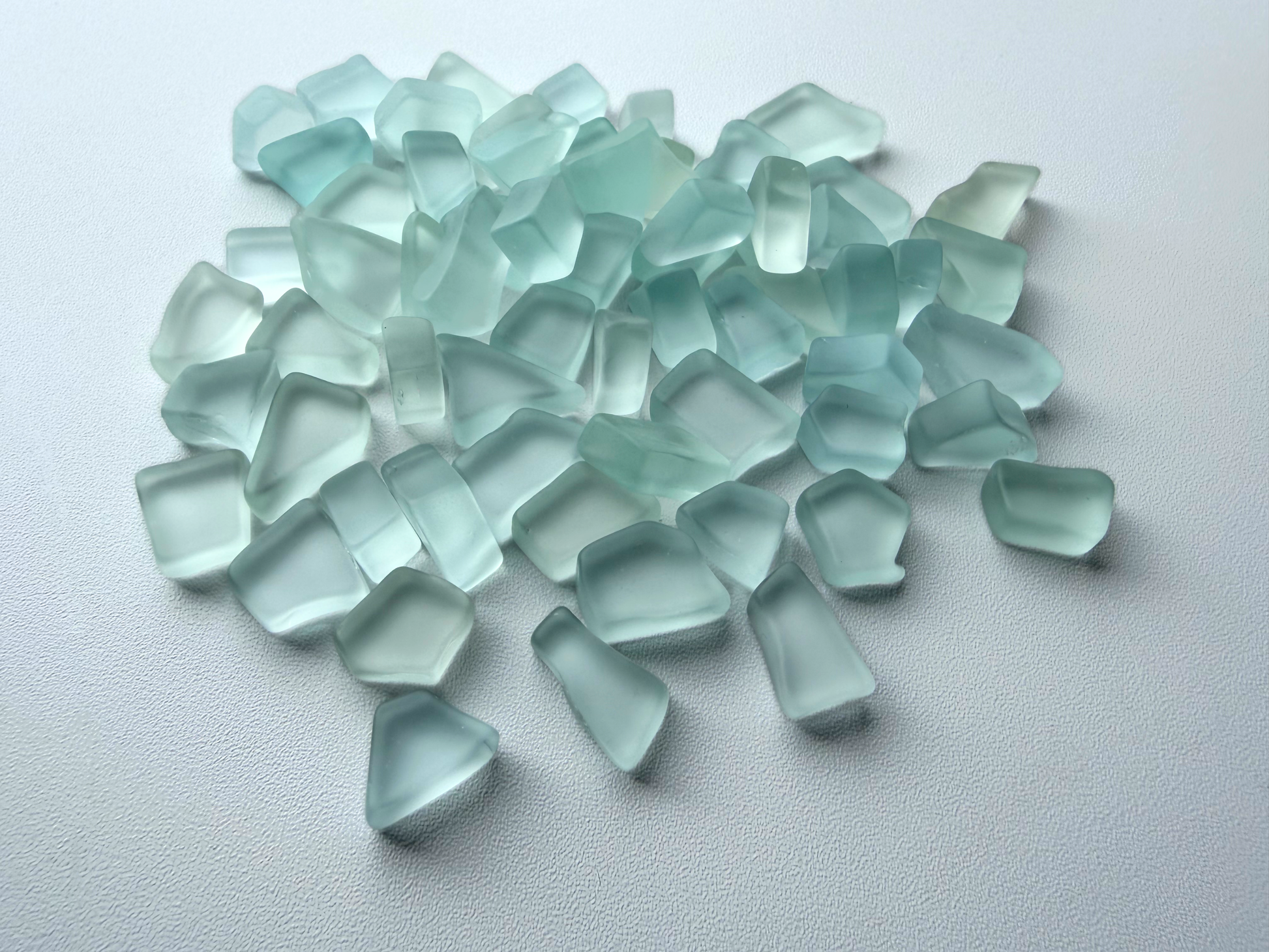 Close-up pile of pale seafoam and sky blue tumbled sea glass, flat on two sides