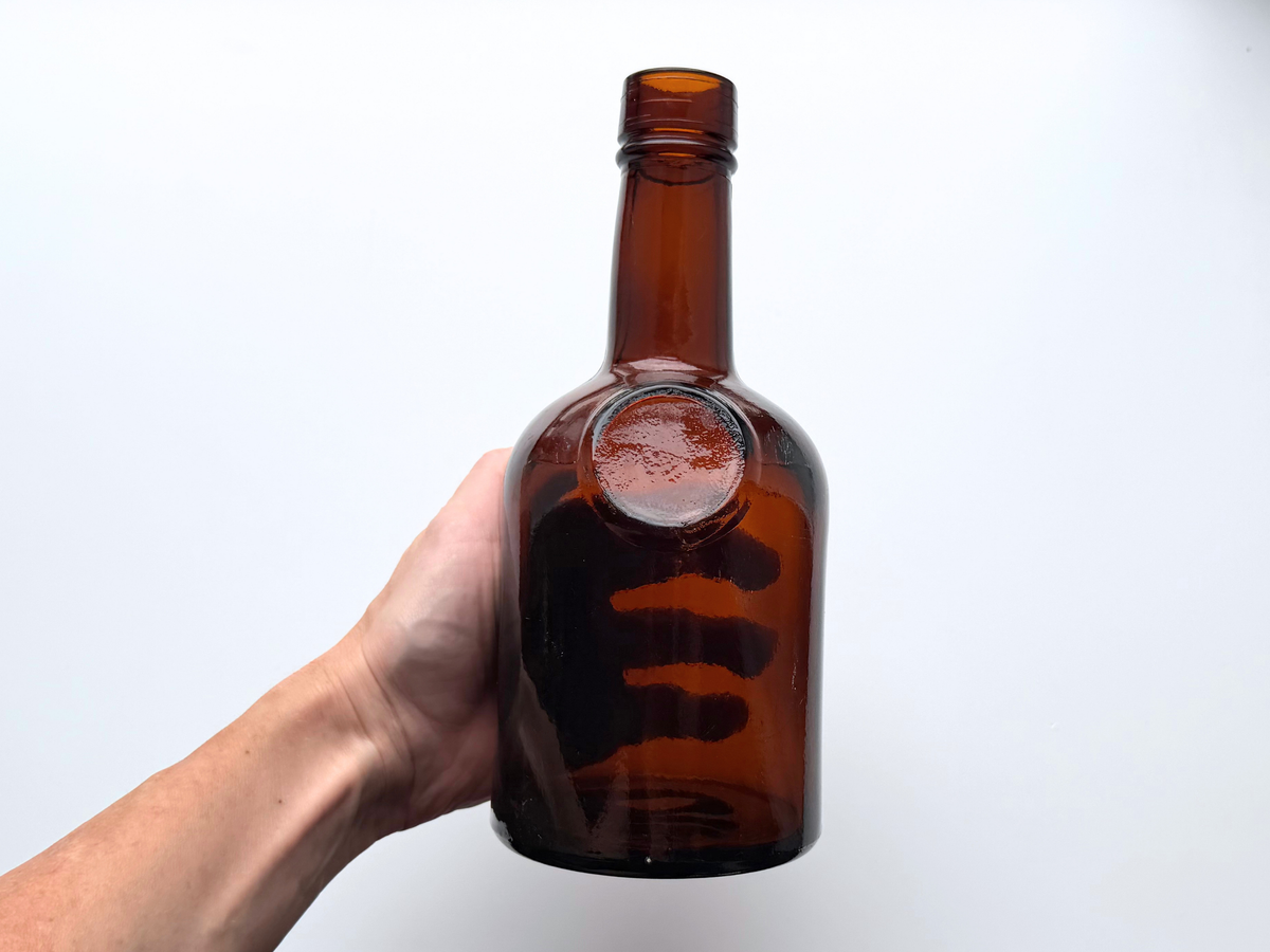 Hand holding a 1953 dark amber glass bottle to show scale and rounded shoulder.