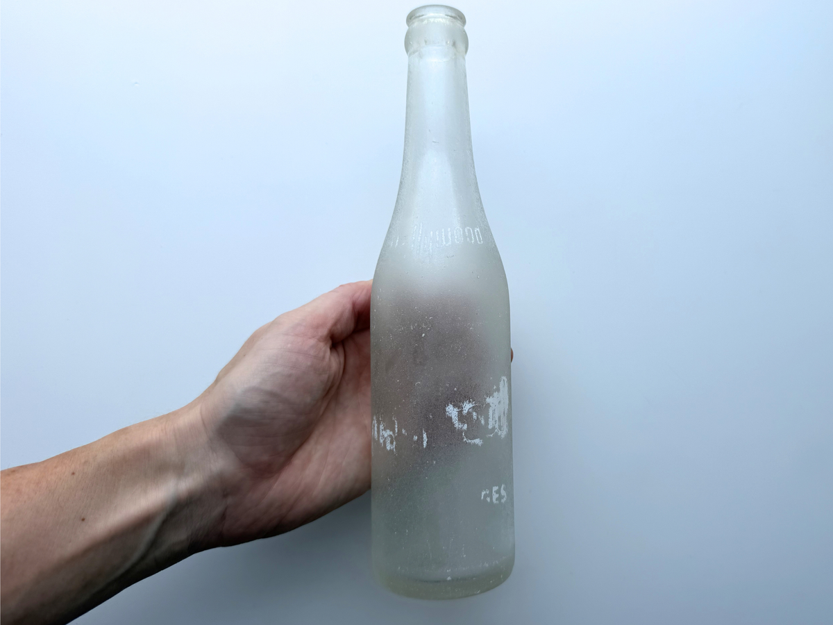Hand holding a sea-worn frosted clear glass Hollywood soda bottle to show its scale and ocean patina