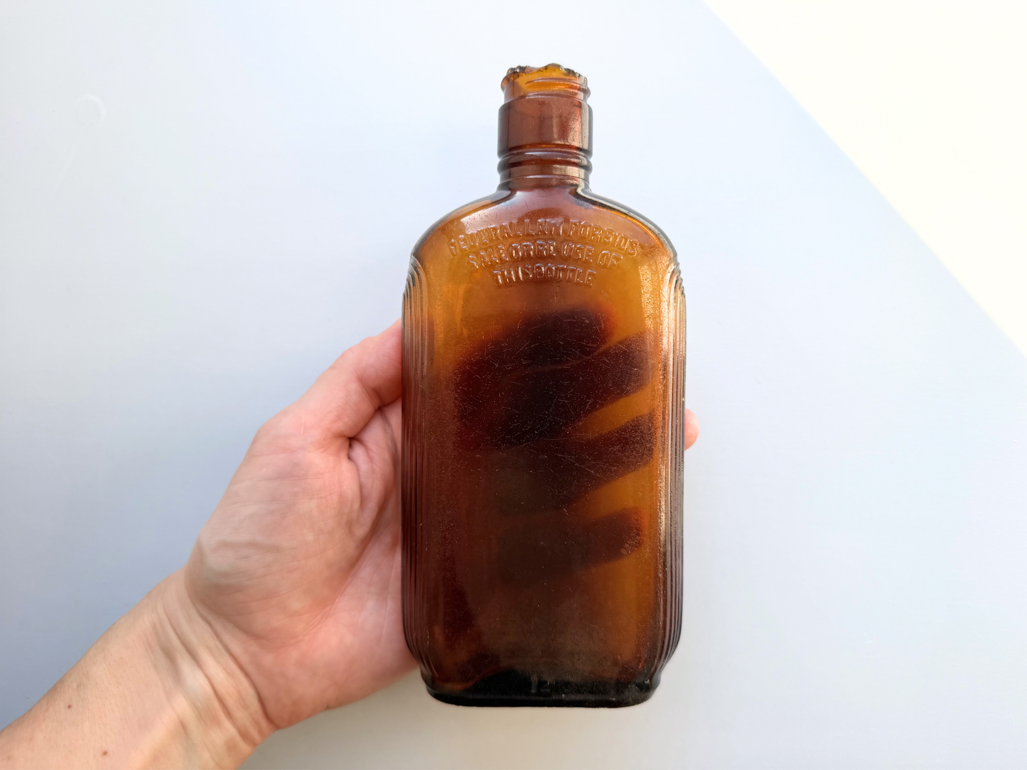 Hand holding a sea-worn amber glass Art Deco flask, showing its compact size