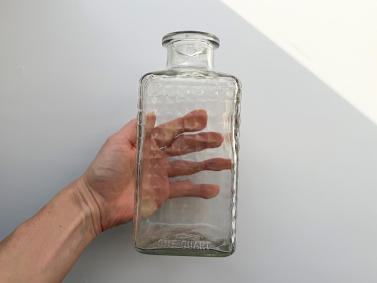 Hand holding a vintage clear glass studded decanter, showing its compact scale