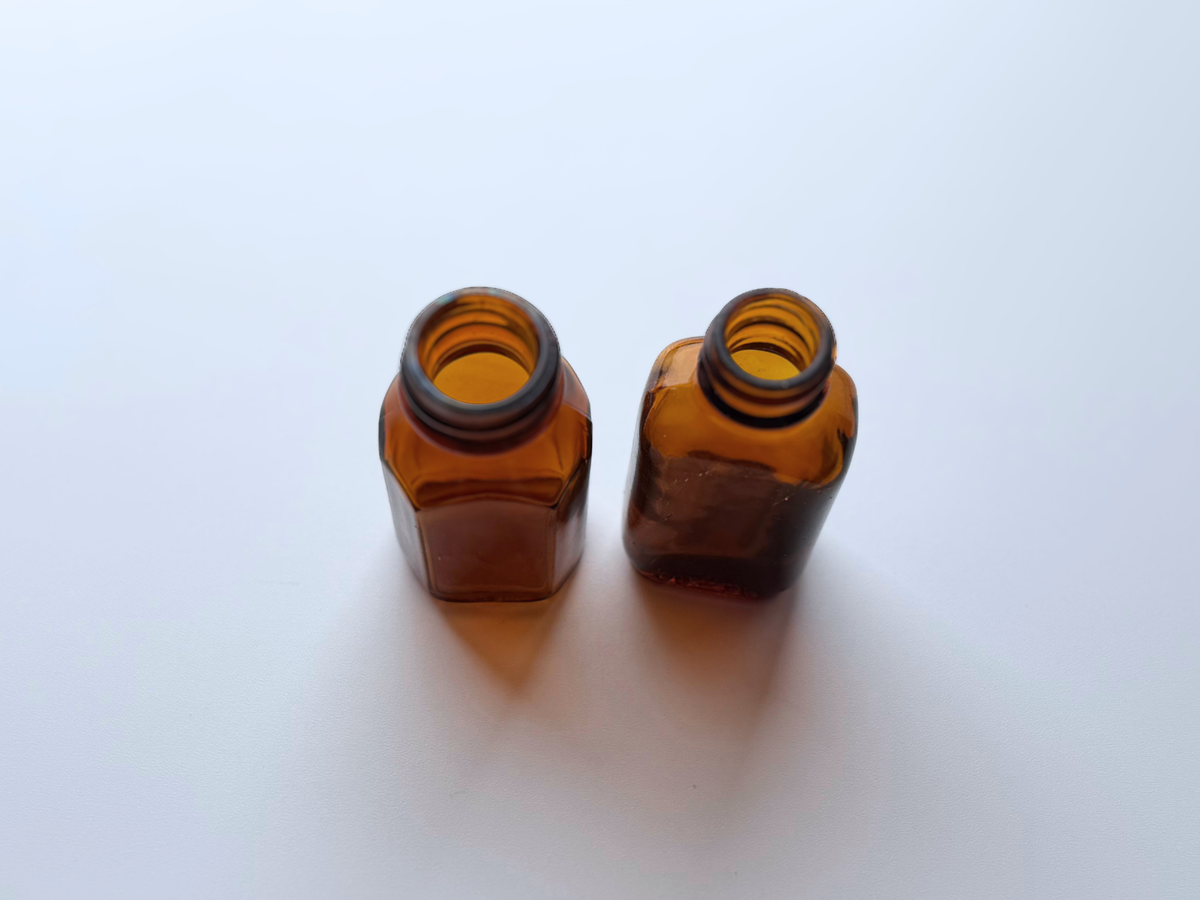 Two 1940s amber glass Duraglas bottles, photographed together on a gradient background.