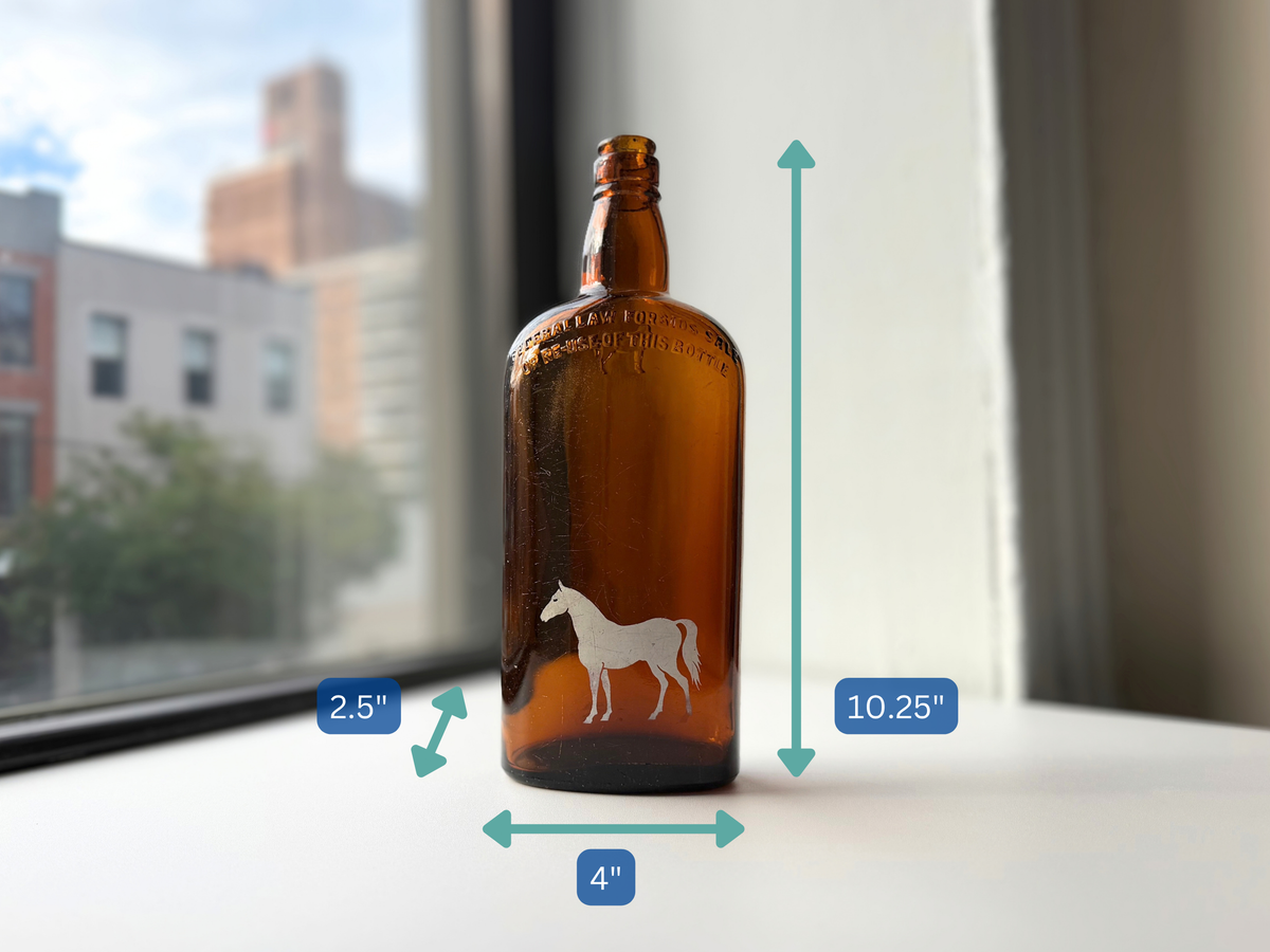 Vintage amber White Horse bottle on a windowsill with measurements marked: 10.25 inches tall, 4 inches wide and 2.5 inches deep.