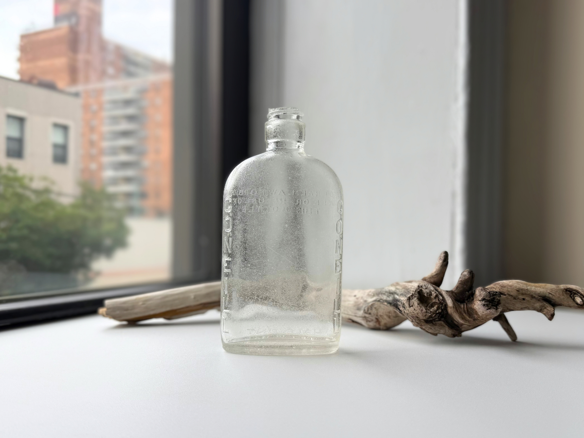 Front of a clear sea-worn G. O'Neill flask on a windowsill, with G.ONEILL embossed vertically along both edges and frosted glass texture.