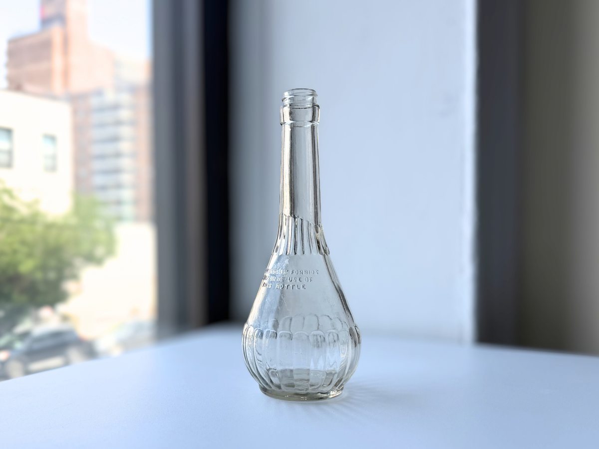 Front view of a ribbed clear glass genie-shaped bottle with a long slender neck