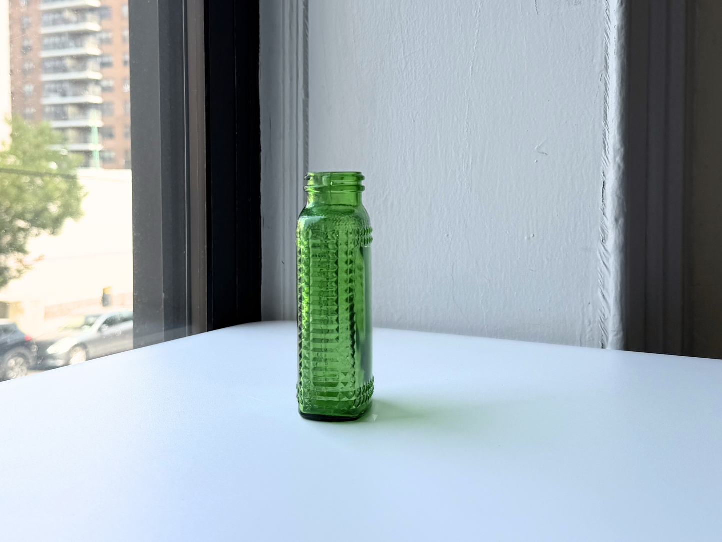 Angled view of a vintage kelly green Airwick hobnail glass bottle