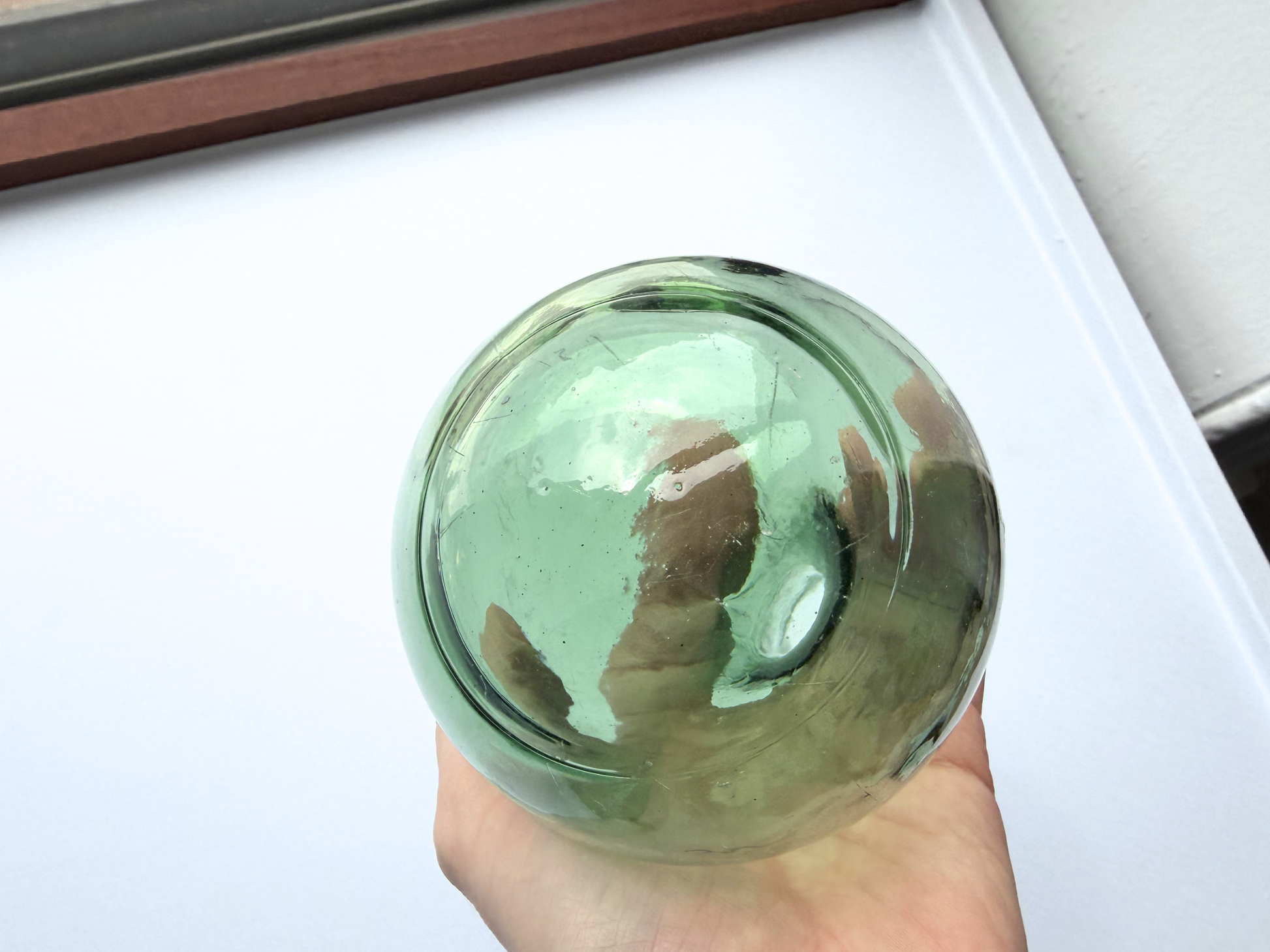 Close-up of a hand holding the rounded base of a vintage green glass teardrop bottle, showing surface texture and bubbles