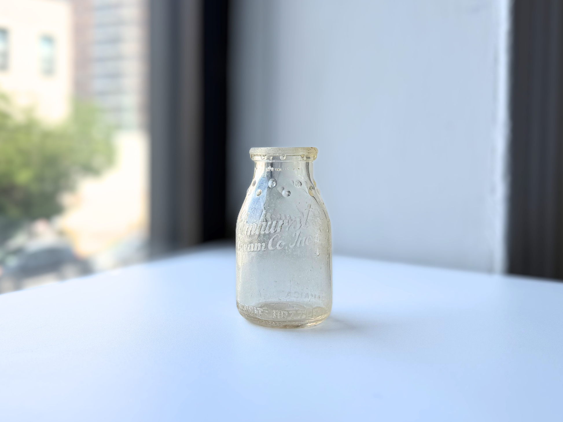 Clear glass Elmhurst Cream Co dairy bottle with sea glass patina displayed on a windowsill