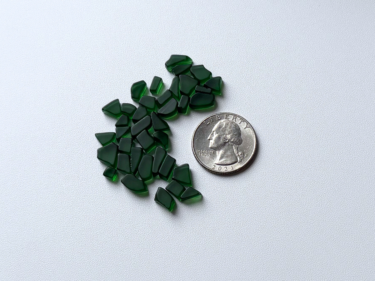 Second angle of a loose pile of dark forest green micro tumbled sea glass, showing the range of shapes and consistent deep green color in this filler mix.
