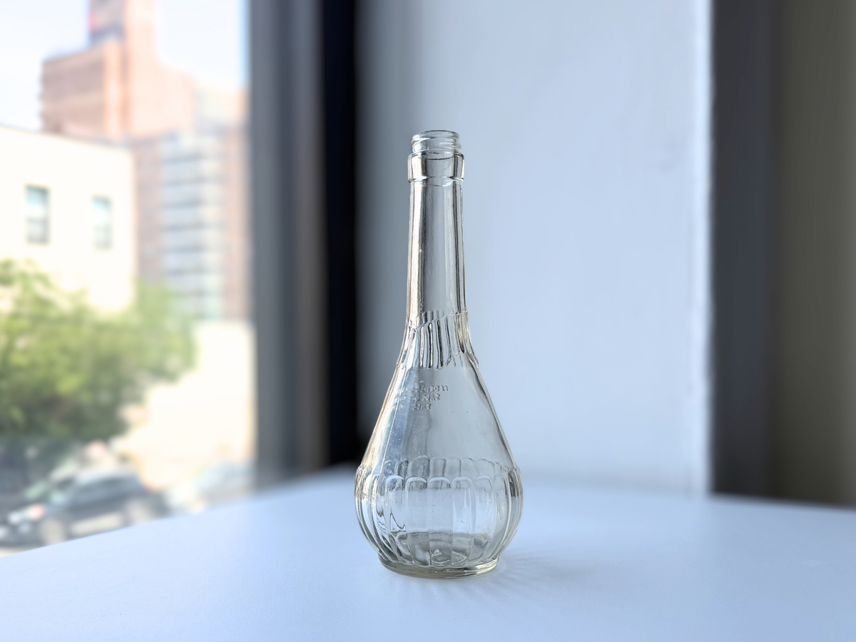 Mid-century genie-shaped clear glass bottle with ribbed lower body, side view on a windowsill