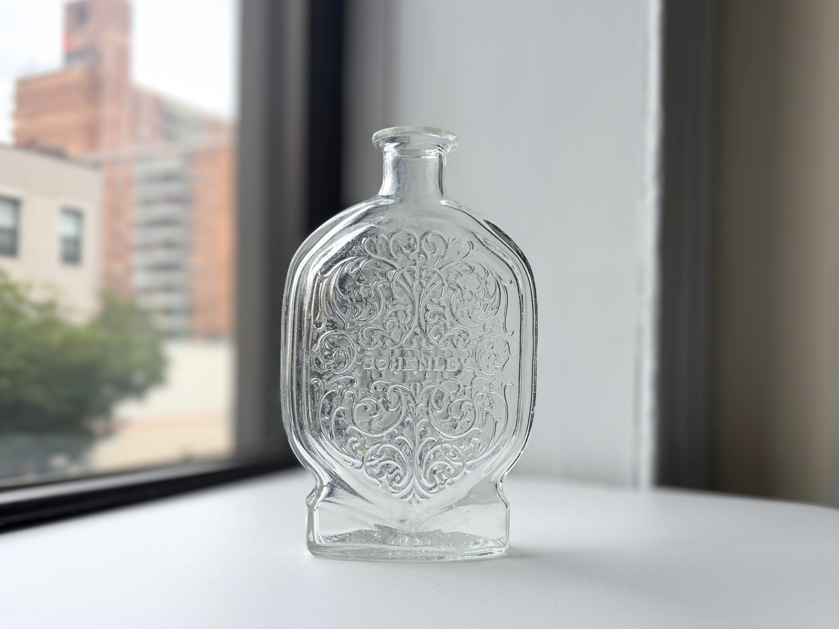 Clear glass Schenley decanter displayed on a windowsill, front view.