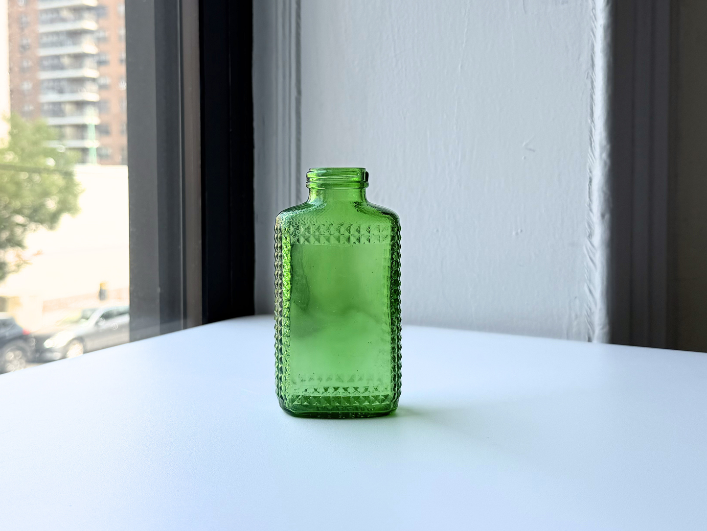 Full body view of a vintage kelly green Airwick hobnail glass bottle on a windowsill