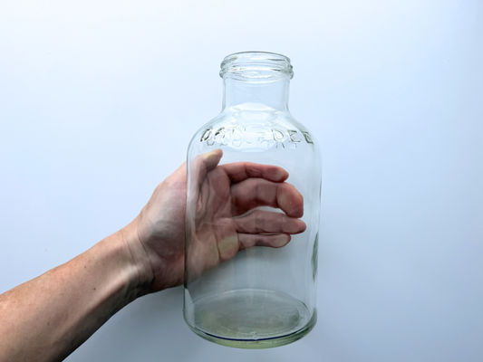 Hand holding a vintage clear glass DAN-DEE jar by the body