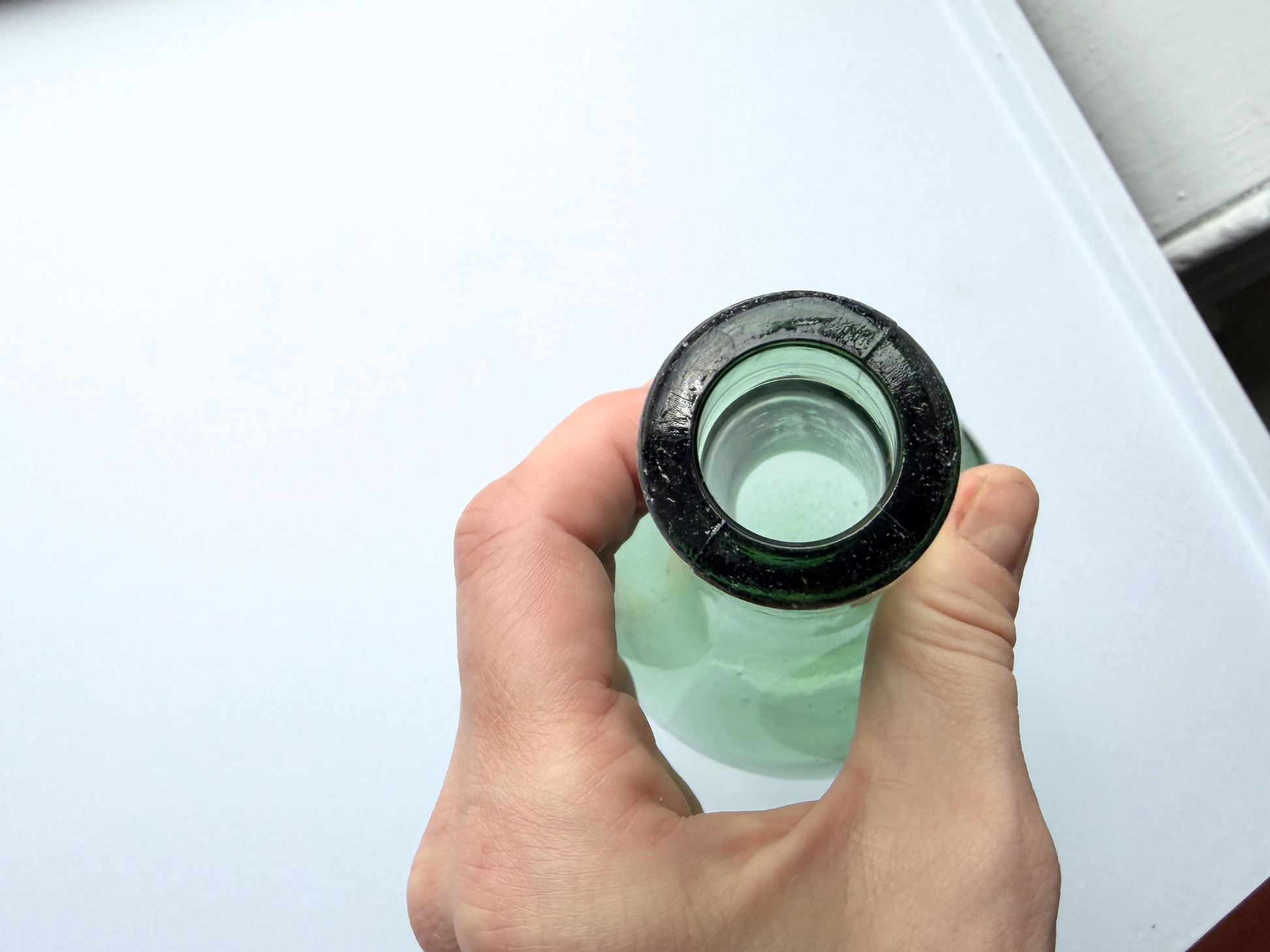Hand holding a vintage green glass teardrop bottle by the neck, showing the open bottle top
