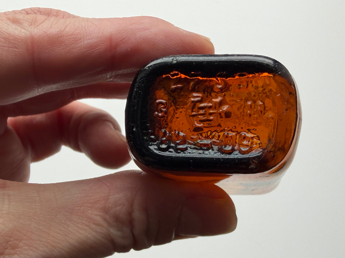 Amber glass bottle base held in hand showing the Anchor Hocking logo.