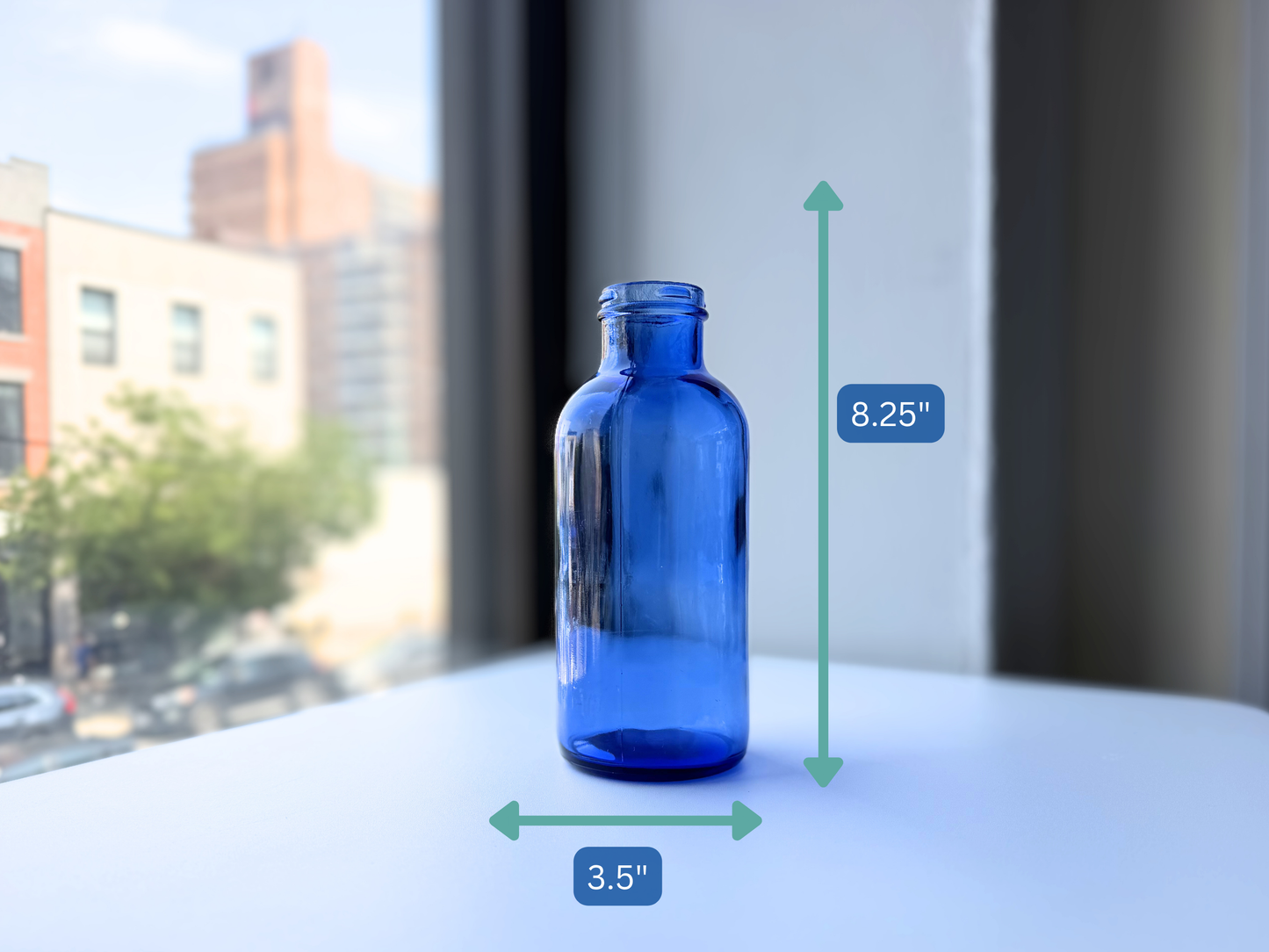 Full body view of a vintage cobalt blue glass pharmaceutical bottle against a window