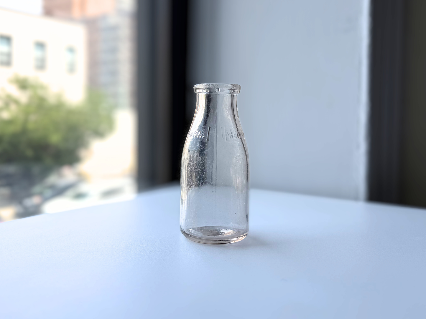 Vintage clear glass Milk for Health milk bottle, full body view against a window