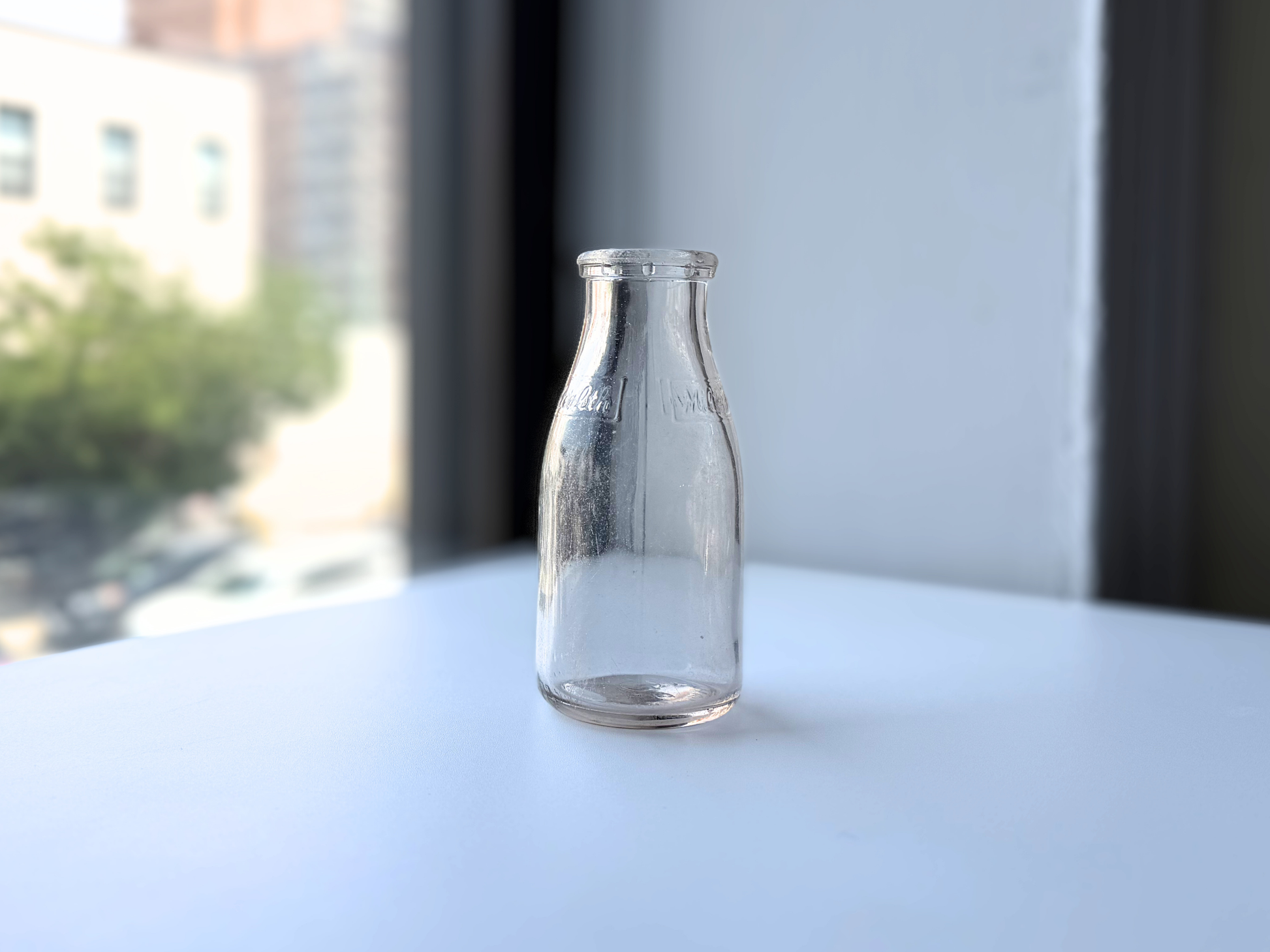 Vintage clear glass Milk for Health milk bottle, full body view against a window
