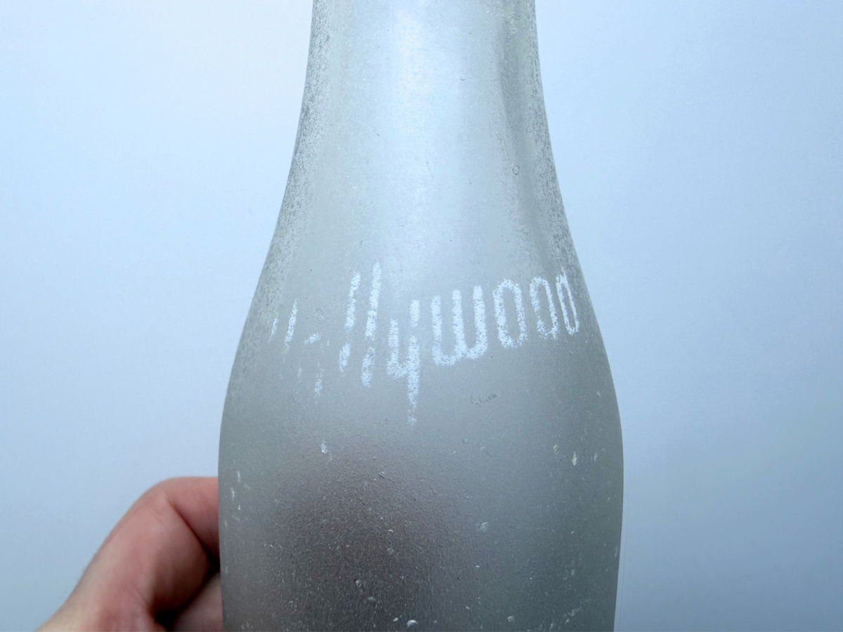 Close view of faded Hollywood lettering on the shoulder of a sea-worn frosted glass bottle