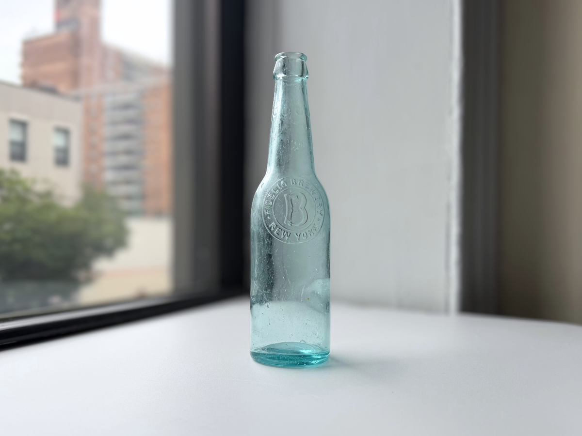 Aqua glass Fidelio Brewery bottle on a windowsill at an angle, showing its slender neck.