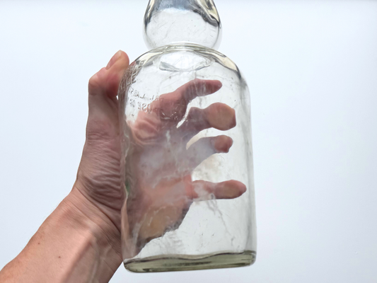 Hand holding the body of a clear glass James Martin & Co. whiskey bottle.