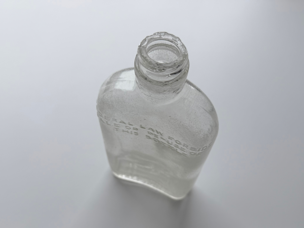Top-down angled view of a clear sea-worn G. O'Neill flask showing the open mouth and Federal Law embossing across the shoulder.