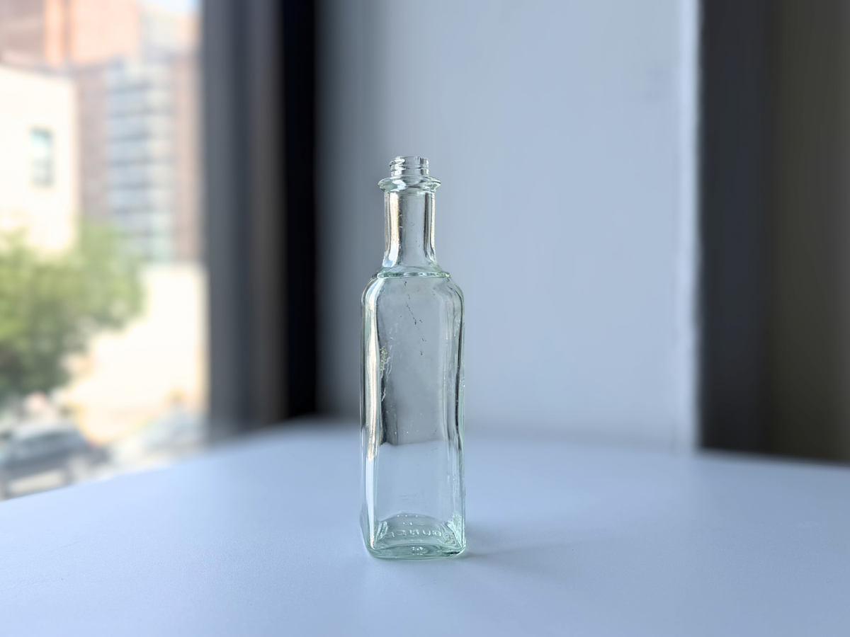 Narrow profile of a vintage greenish-blue glass hair dressing bottle with a rounded shoulder and banded neck