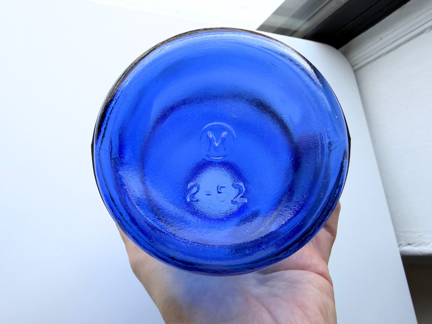 Hand holding a vintage cobalt blue glass pharmaceutical bottle, viewed from above into the opening