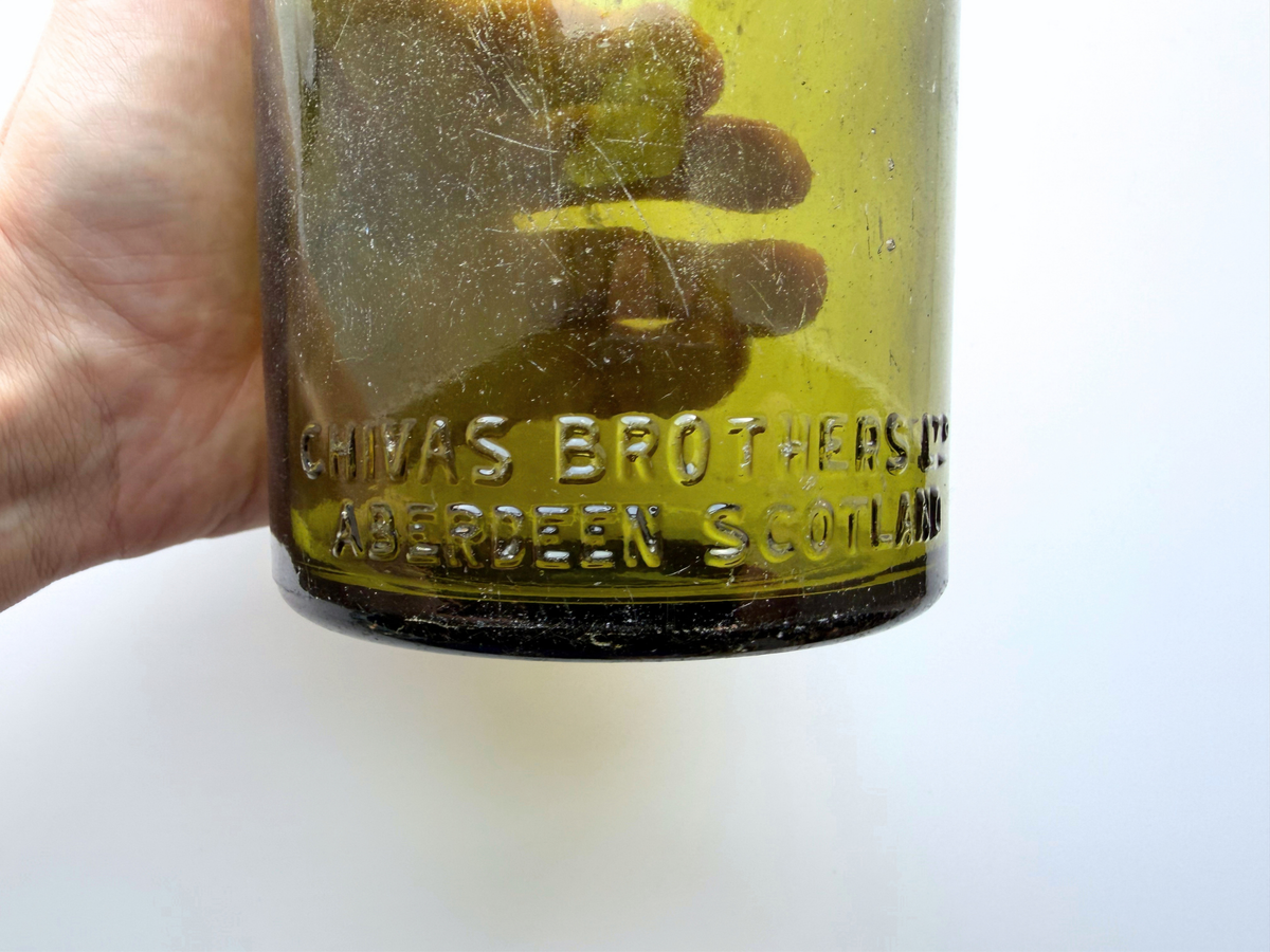 Close view of the embossed Chivas Brothers Ltd Aberdeen Scotland lettering on a green glass bottle held in hand