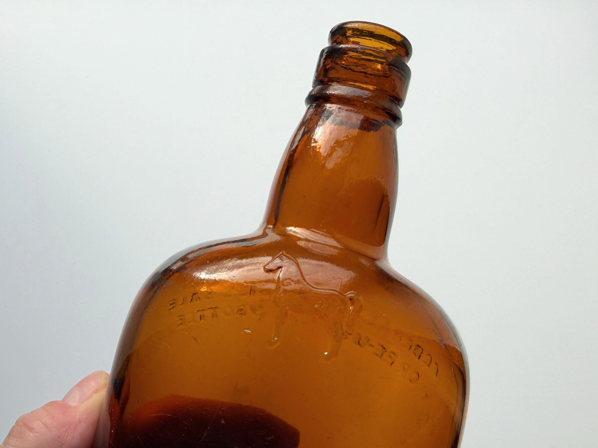 Shoulder of a vintage amber White Horse bottle with a small embossed horse and raised lettering reading FEDERAL LAW FORBIDS SALE OR RE-USE OF THIS BOTTLE.
