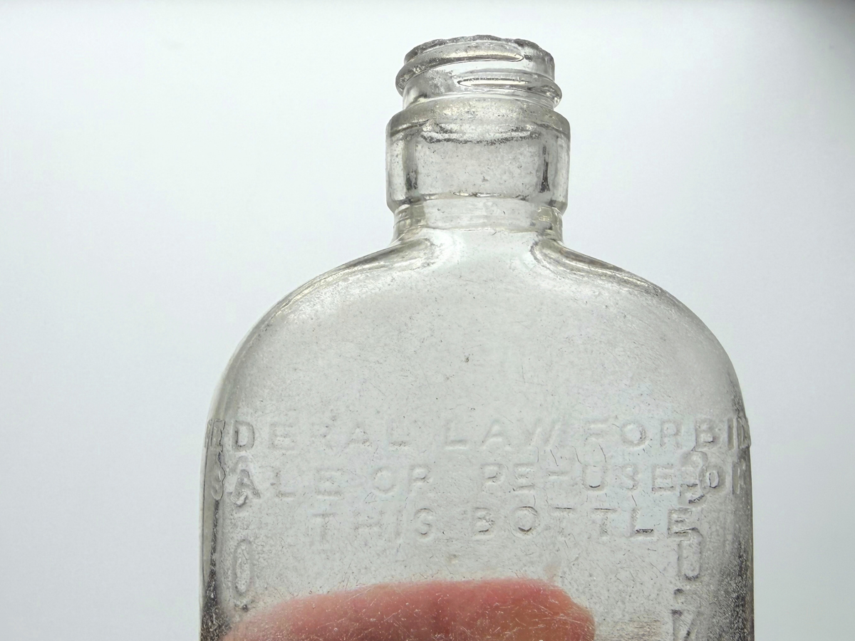 Close-up of the neck and shoulder of a clear sea-worn G. O'Neill flask with raised Federal Law Forbids Sale or Reuse of This Bottle embossing.