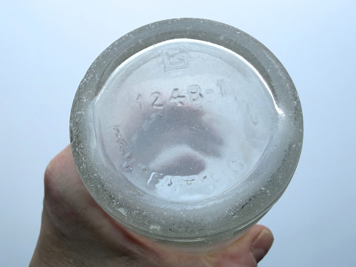 Base of the Hollywood soda bottle held up to show the G in a square glassmaker mark and frosted sea-worn edge