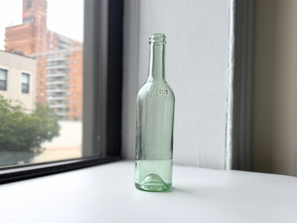Pale green glass bottle displayed on a windowsill with Brooklyn brownstones in the background.