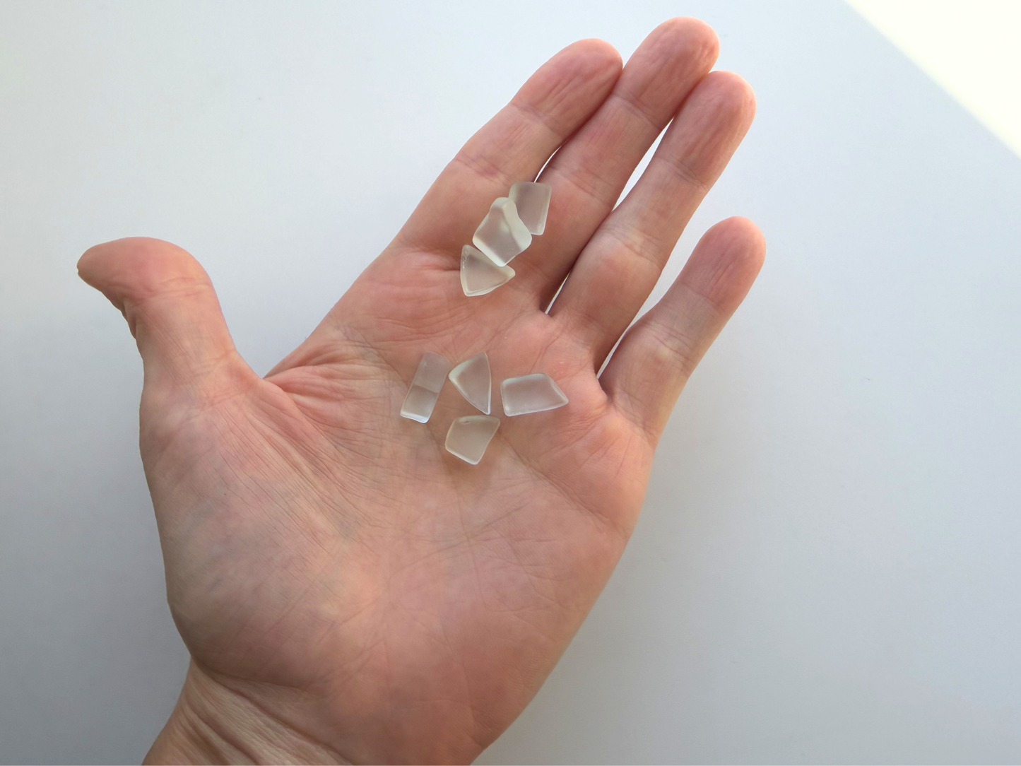 Handful of pale seafoam and sky blue tumbled sea glass pieces held for scale