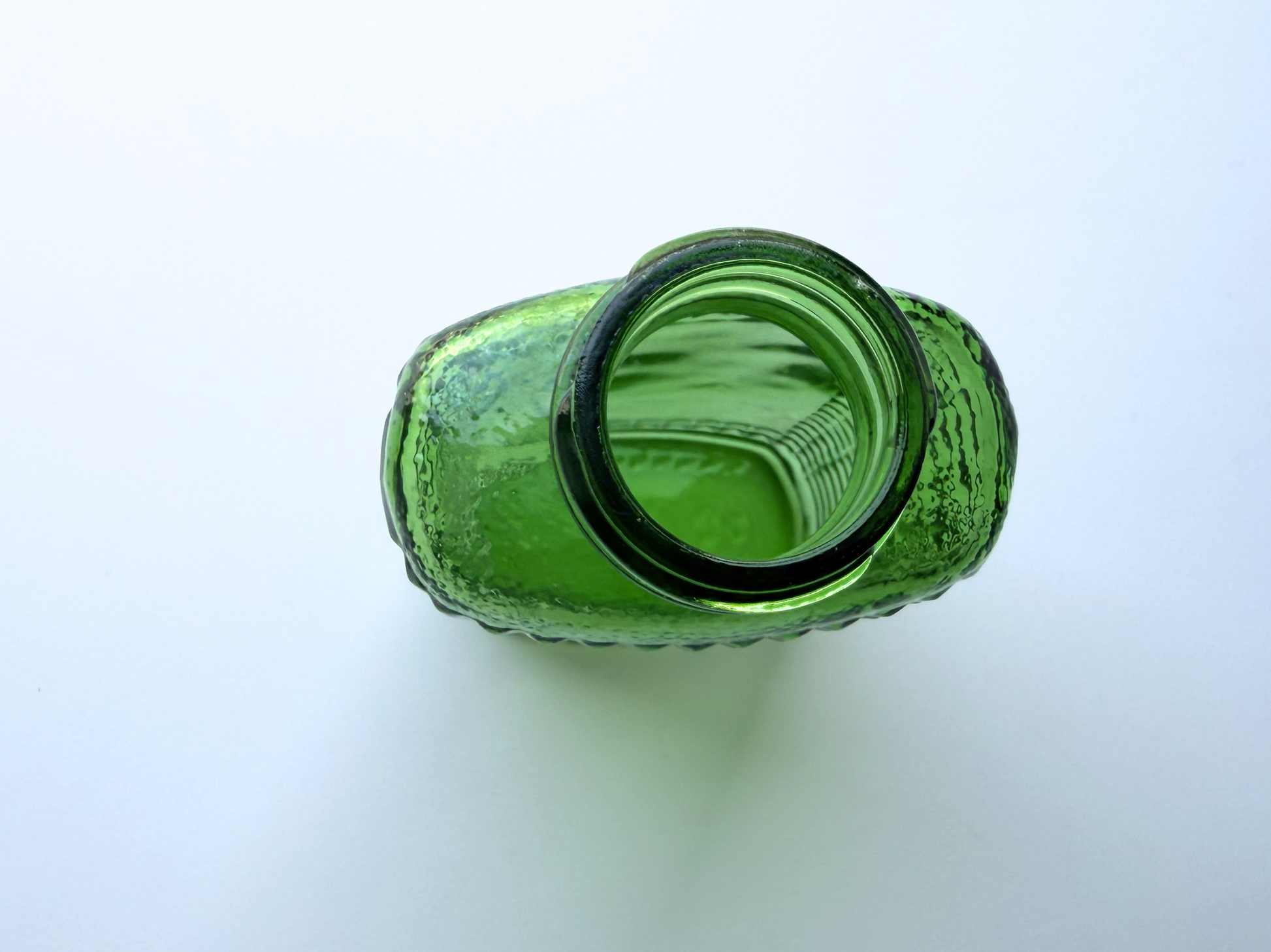 Hand holding a vintage kelly green Airwick hobnail glass bottle