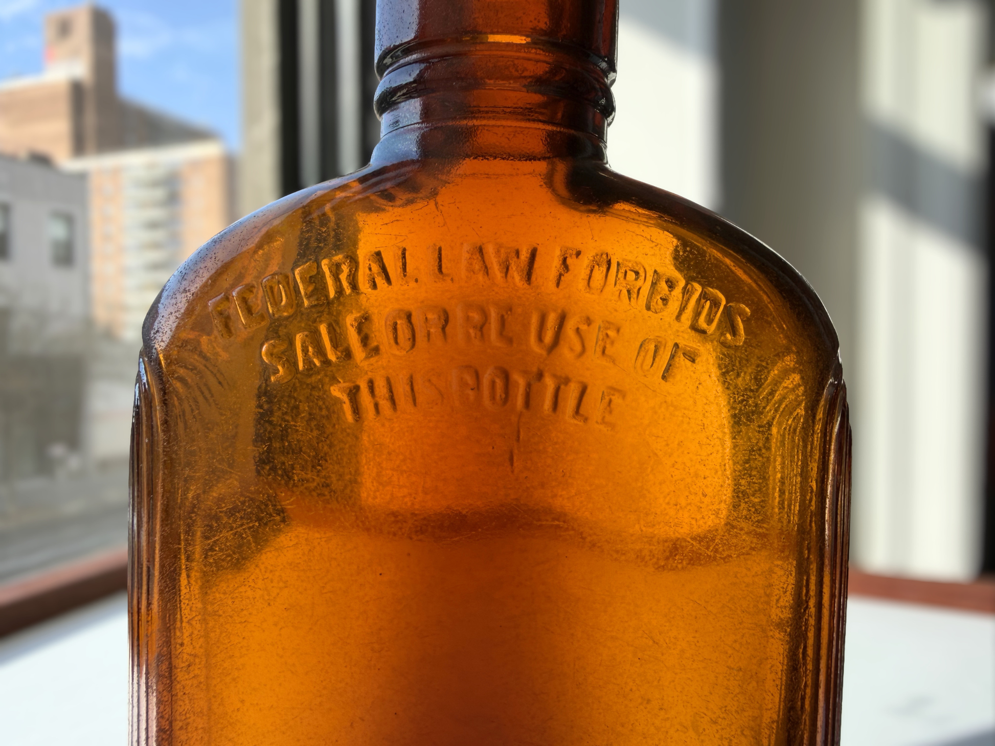 Close view of a sea-worn amber glass flask showing faint raised lettering beneath the frosted patina