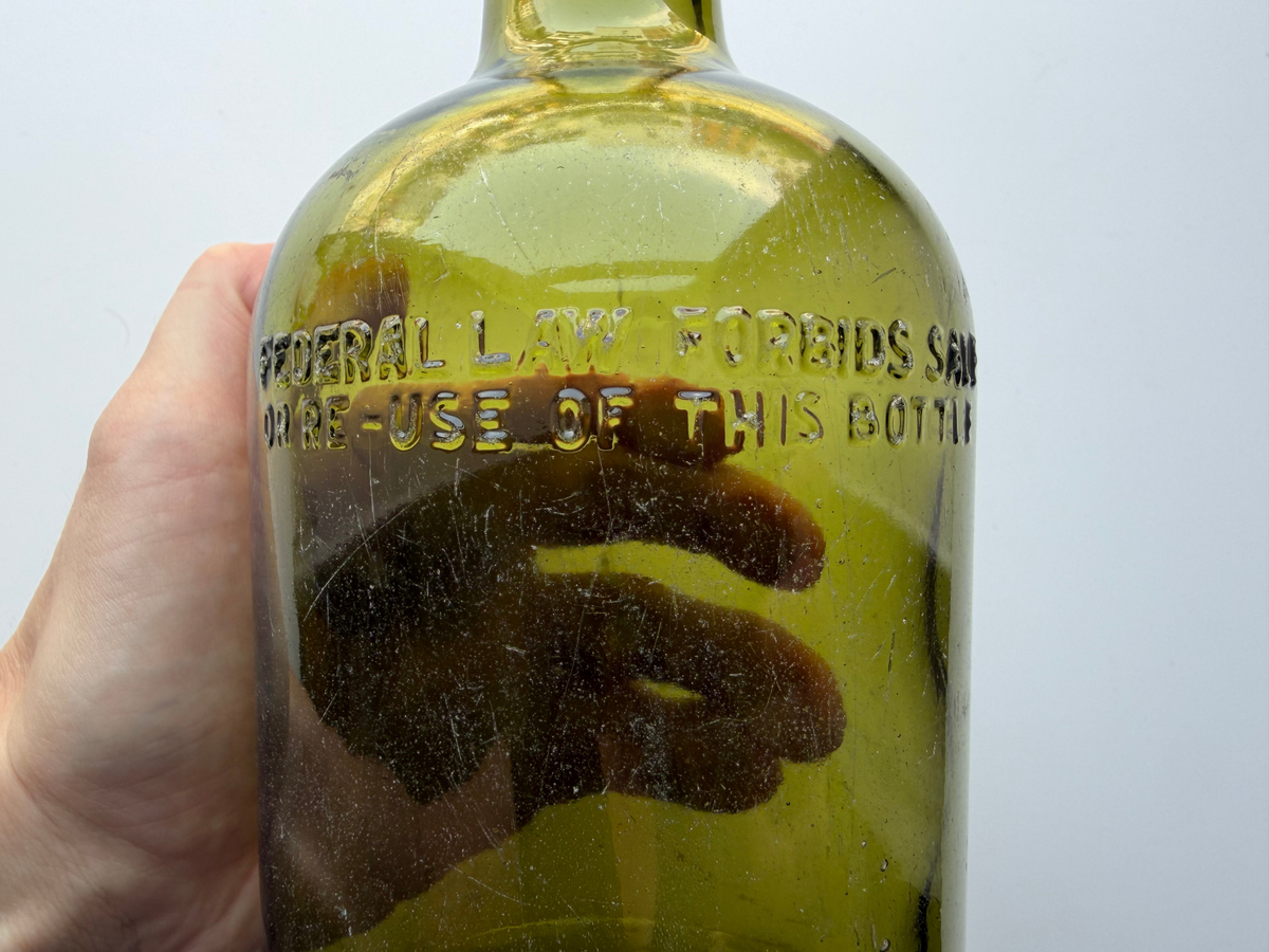 Embossed Federal Law forbids sale or reuse lettering on the shoulder of a green glass bottle held in hand