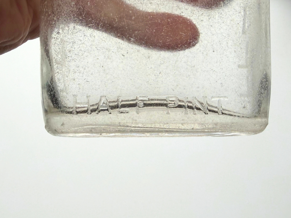 Close-up of the base of a clear sea-worn G. O'Neill flask showing the embossed words Half Pint and a frosted, softly worn surface.