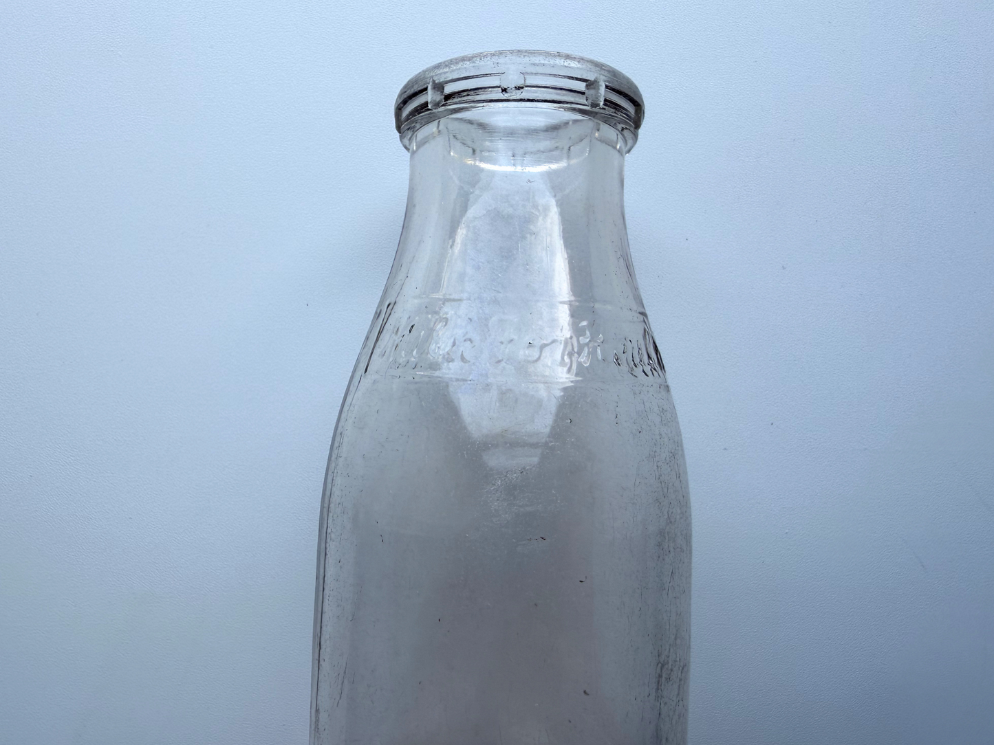 Close-up of the neck and shoulder of a vintage Milk for Health glass milk bottle, showing light haze