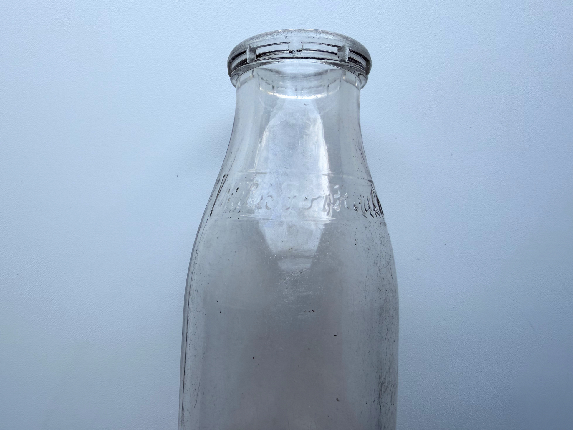 Close-up of the neck and shoulder of a vintage Milk for Health glass milk bottle, showing light haze